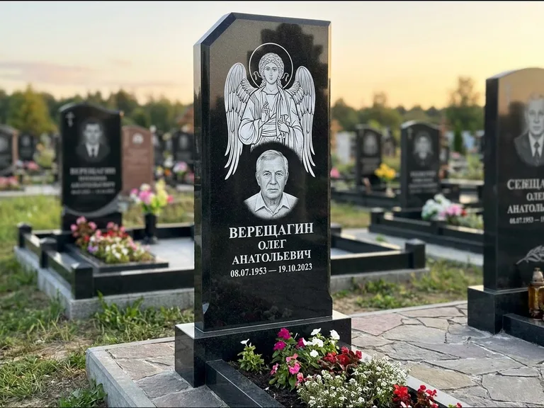 Памятник с гравировкой иконы: стела с резным навершием и нимбом в золоте — гравировка образа Спасителя, высокие разросшиеся туи полукругом, работа «Мельникова» в Санкт-Петербурге