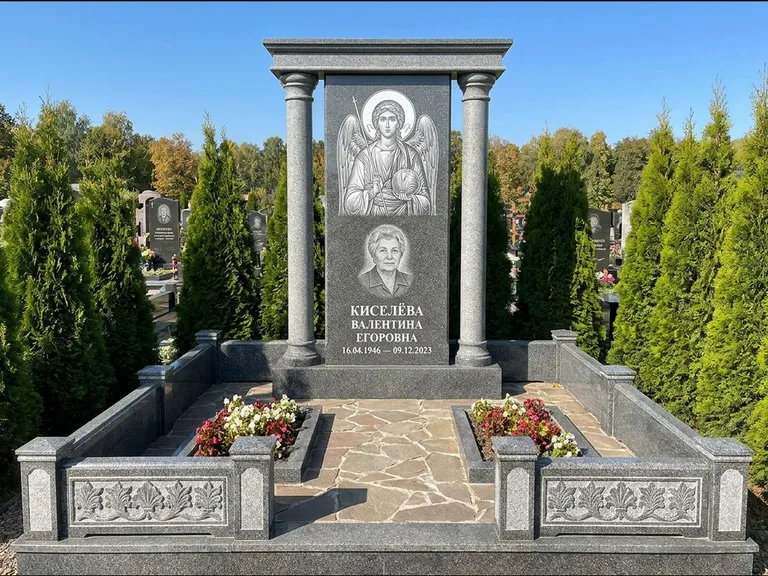 Памятник с гравировкой иконы: массивная стела с двускатным навершием-домиком — гравировка Николая Чудотворца, живая изгородь из туи, работа «Журавлёв» в Санкт-Петербурге