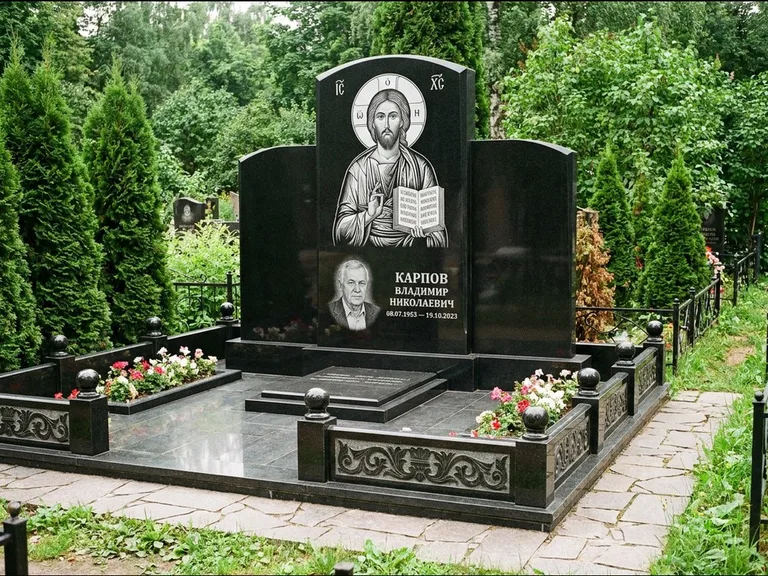 Памятник с гравировкой иконы: широкая панорамная стела с золочёным нимбом — гравировка образа Матроны Московской, цветник с белыми хризантемами, работа «Мельникова» в Санкт-Петербурге