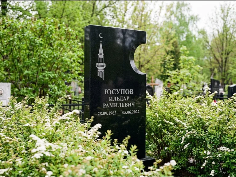 Мусульманский памятник с гравировкой мечети: стела с боковым вырезом в форме полумесяца — гравировка минарета с полумесяцем, низкие кусты спиреи в цвету, работа «Юсупов» в Санкт-Петербурге