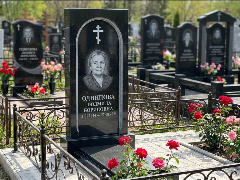 Памятник из чёрного гранита — скромная невысокая стела с крестом с терновым венцом, работа «Лаврентьева» в Санкт-Петербурге